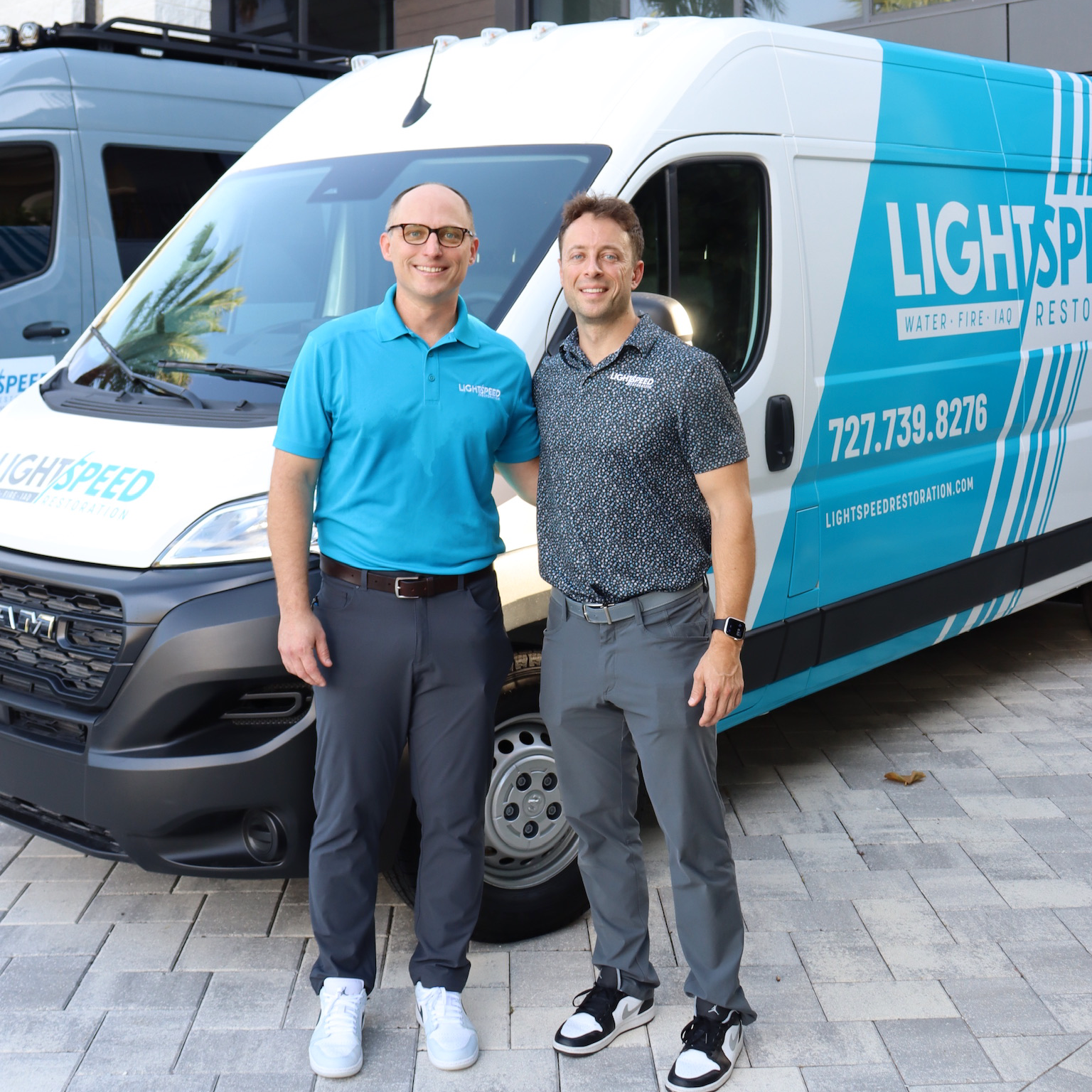 Owners of Lightspeed Restoration standing in front of a branded company van outside a commercial building.